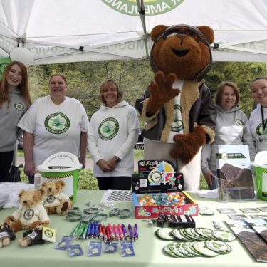 gnaas fundraisers and volunteers with merchandise at stall with miles the bear mascot